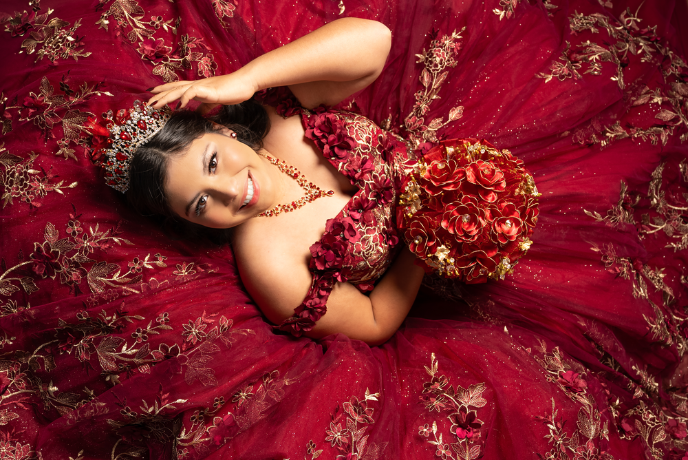 Person in red embellished ball gown lying on floor for dramatic portrait.