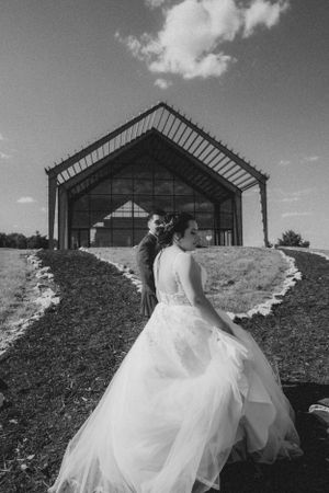 Black and white wedding photo with flowing dress against modern architectural backdrop.