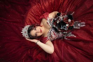 Overhead view of person in red formal gown with silver accessories laying on red fabric.