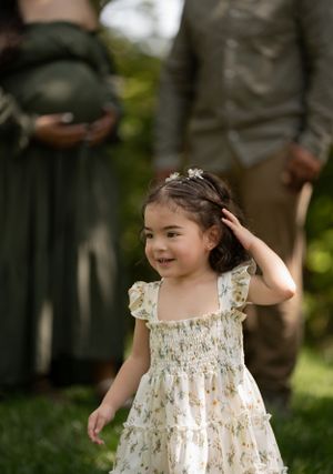 A small child in a floral dress plays outdoors on a sunny day.
