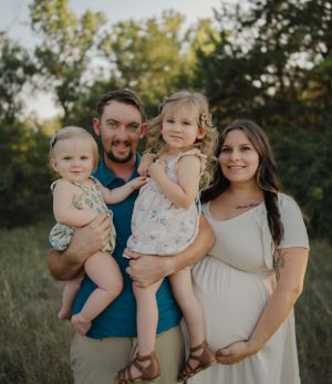 A family portrait outdoors showing parents with two small children in casual attire.
