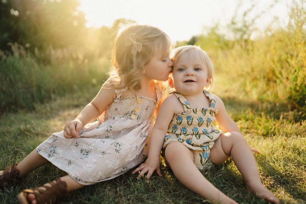 Two young children sitting together in grass during golden sunset.