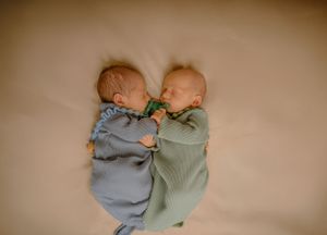 Two babies in gray and sage green outfits lying side by side.