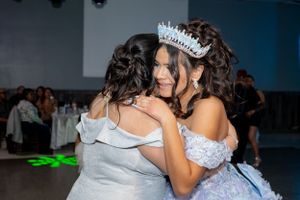Two people embracing at formal event wearing white gowns and tiara.