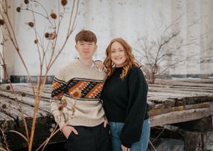 Casual outdoor portrait of couple wearing sweater and black coat in winter setting.