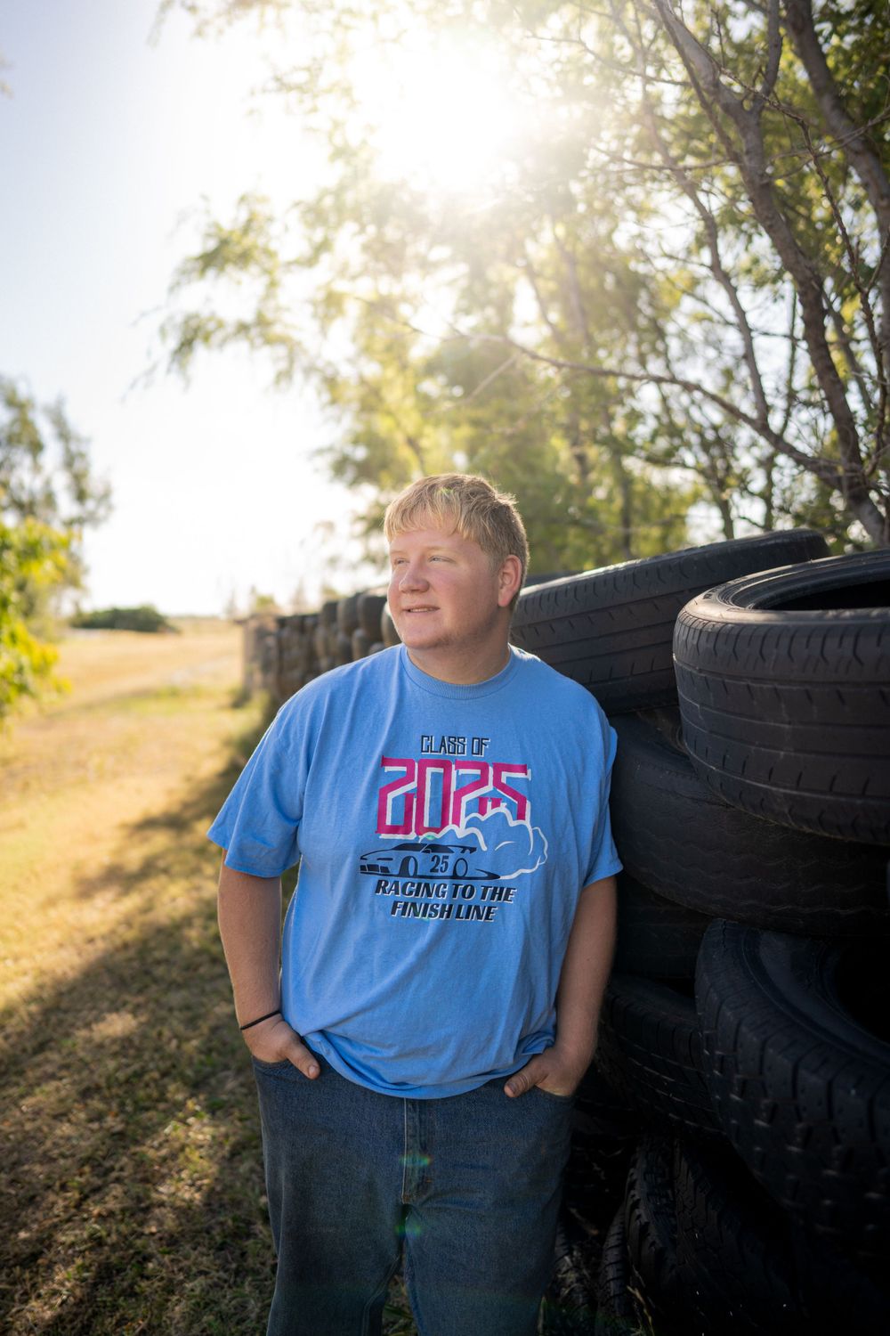 A person in a blue t-shirt stands beside stacked tires on a sunny day.