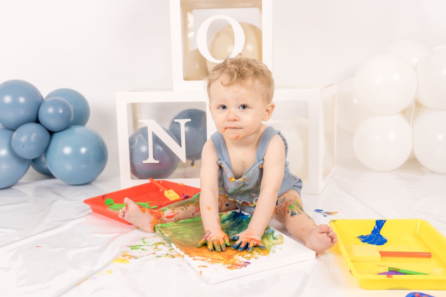 Baby in blue onesie crawls on white floor during developmental milestone photo session.