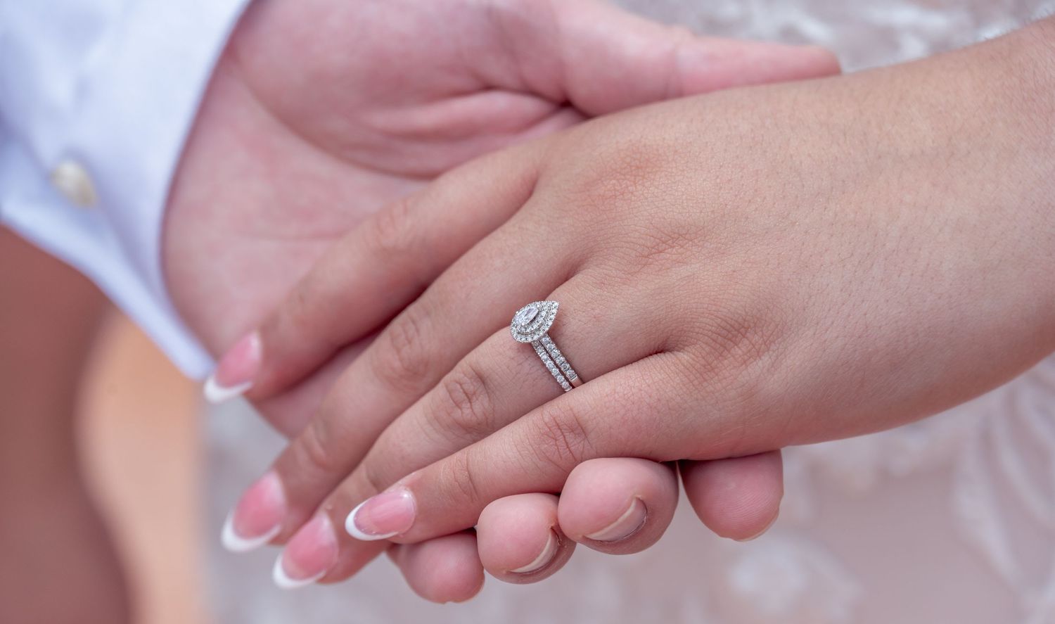 Bride and groom holding hands wearing a white gold solitaire diamond engagement ring on a manicured finger.
