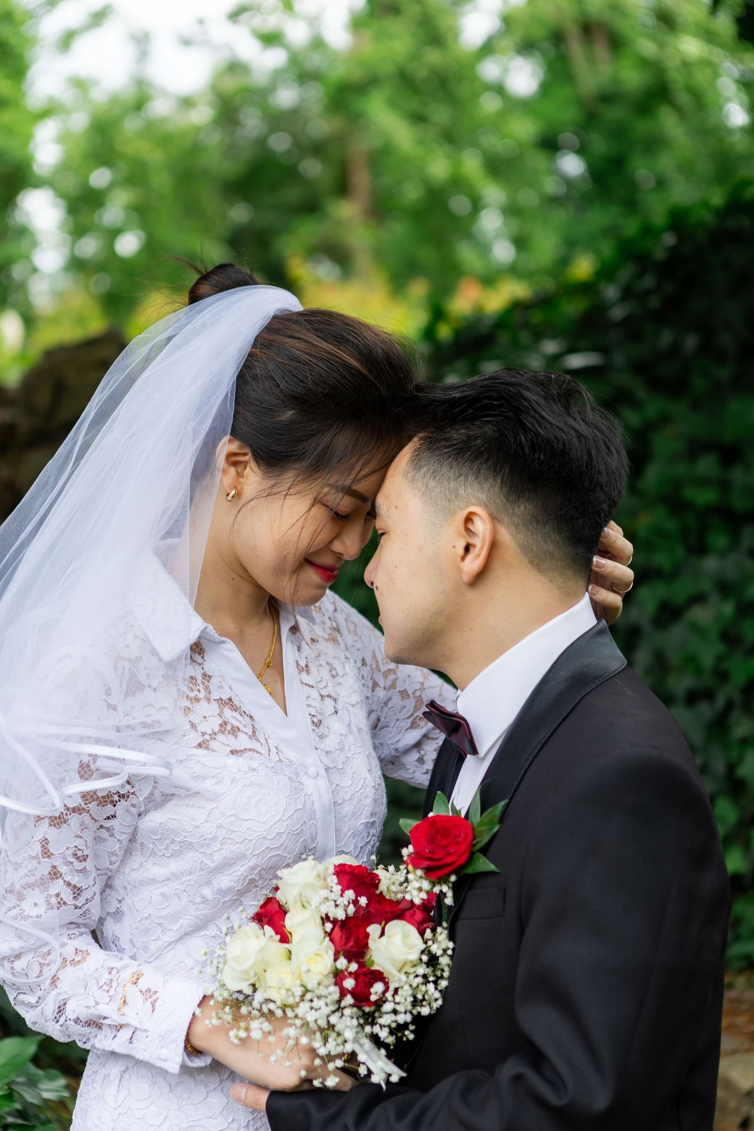 Romantic wedding couple shares tender moments in garden setting with red and white floral bouquet.