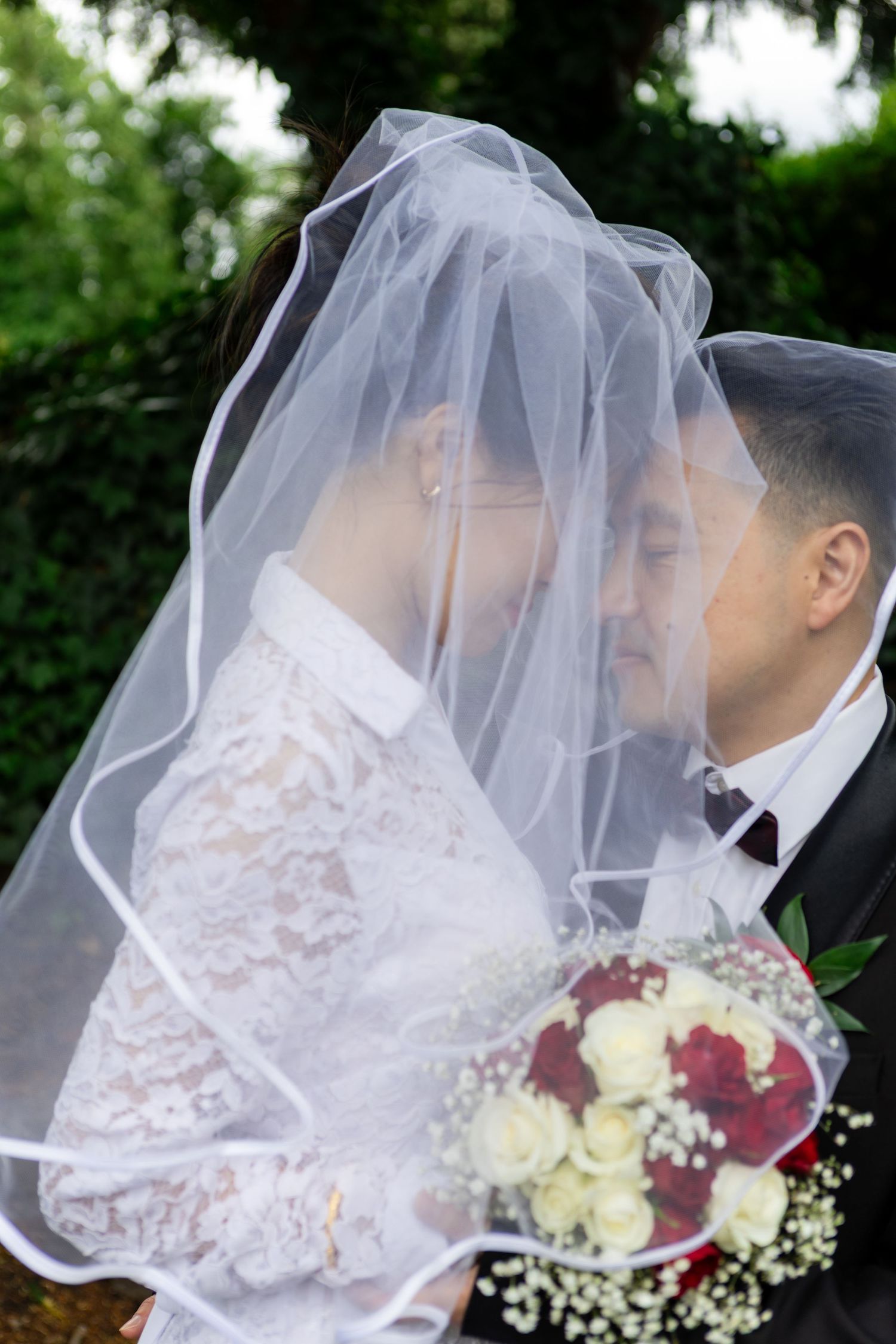 A romantic wedding moment under a veil with a bouquet of red and white roses with baby's breath.