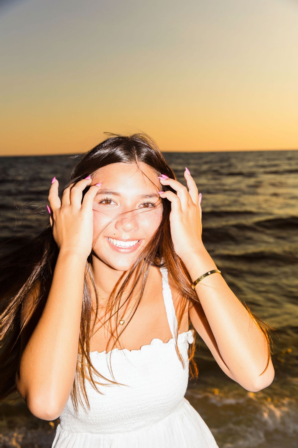 Beach portrait at sunset with someone smiling and adjusting their hair by the ocean.