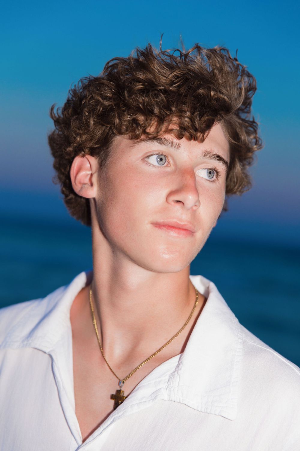 Portrait against ocean backdrop with curly hair and white shirt in evening light.