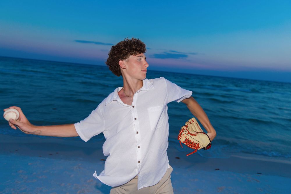 Action shot of someone playing baseball on the beach at dusk with ocean background.