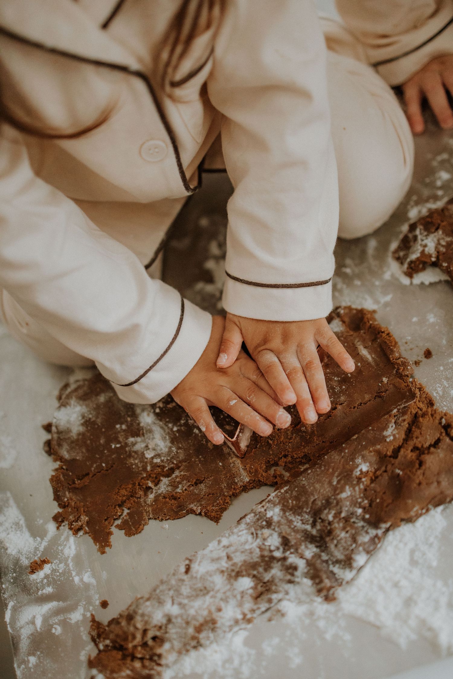 Child in white pajamas pressing chocolate cookie dough on a floured surface during holiday baking.