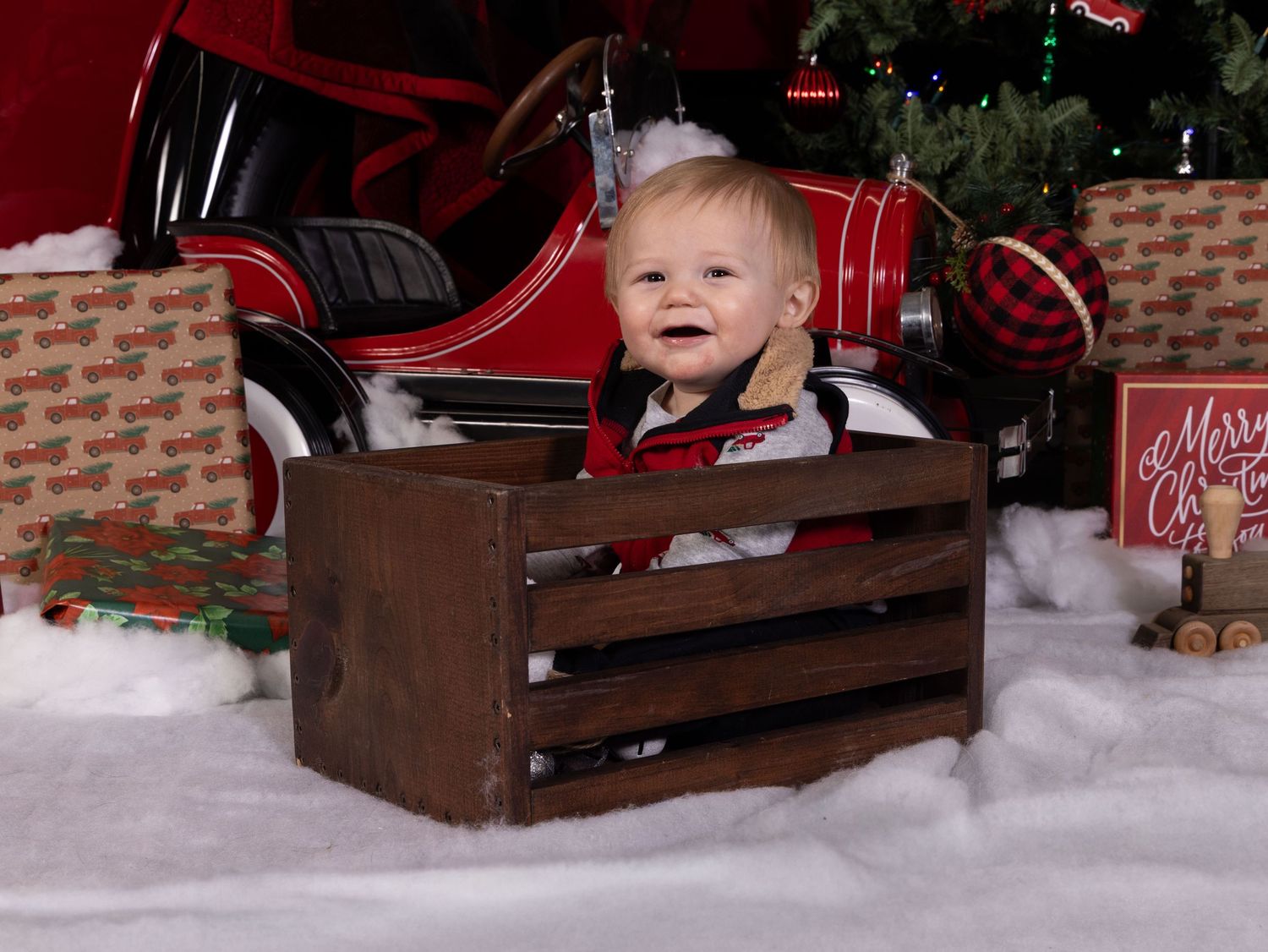 A festive Christmas photo setup with a wooden sleigh prop surrounded by artificial snow and holiday decorations.