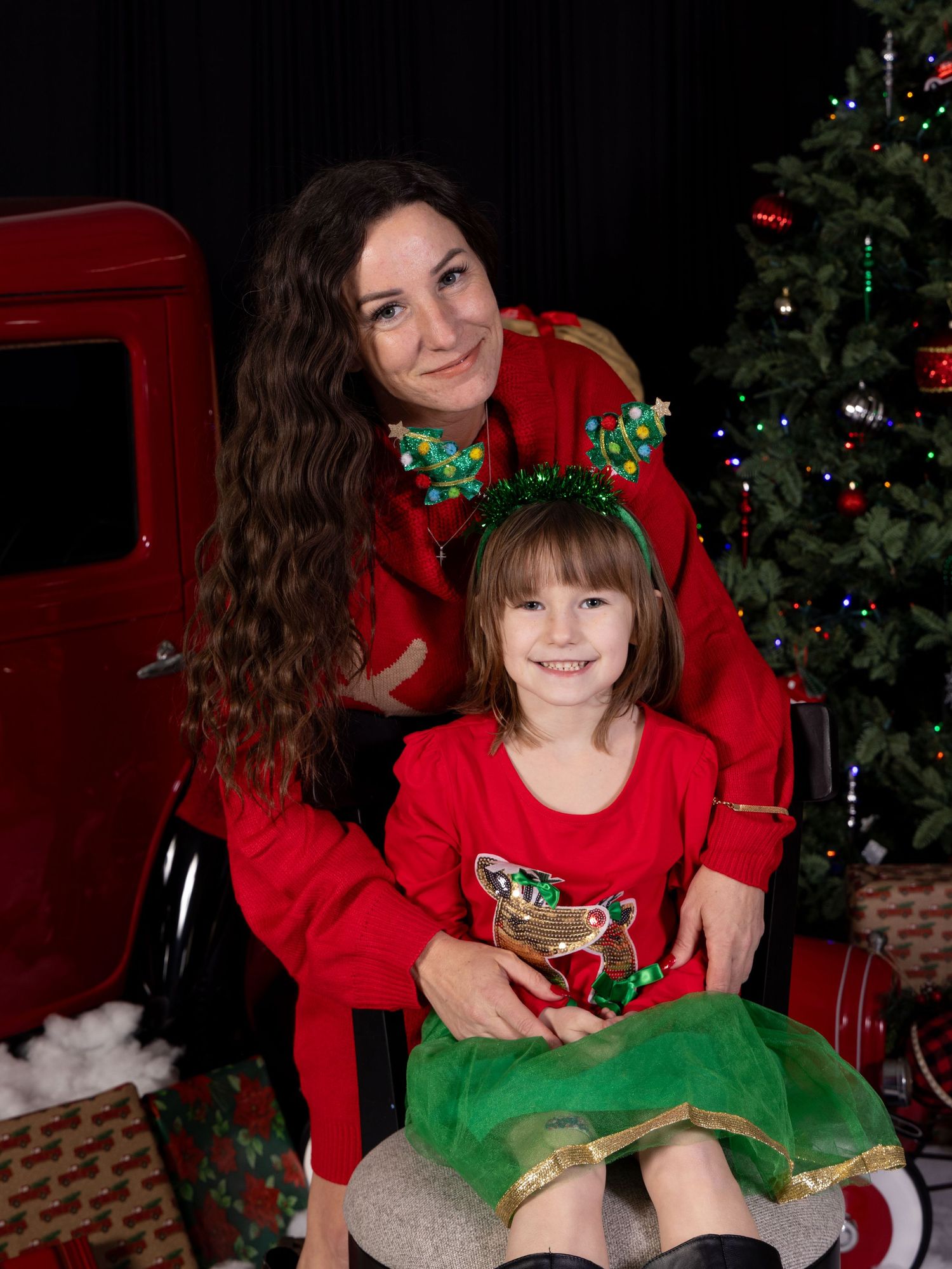 A festive holiday photoshoot shows two people in matching red and green outfits posing in front of a decorated Christmas tree.