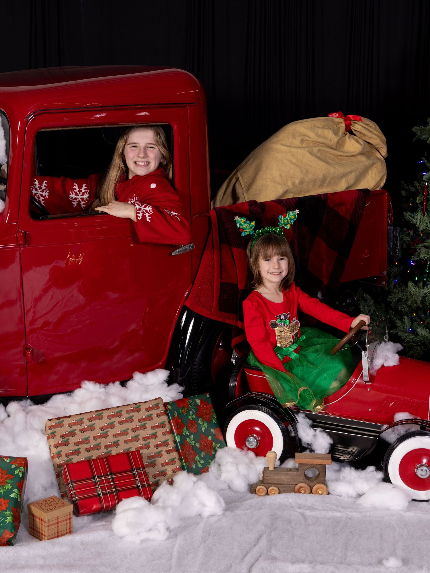 Festive Christmas scene with vintage red toy truck, presents wrapped in plaid paper, and holiday decorations on snowy display.