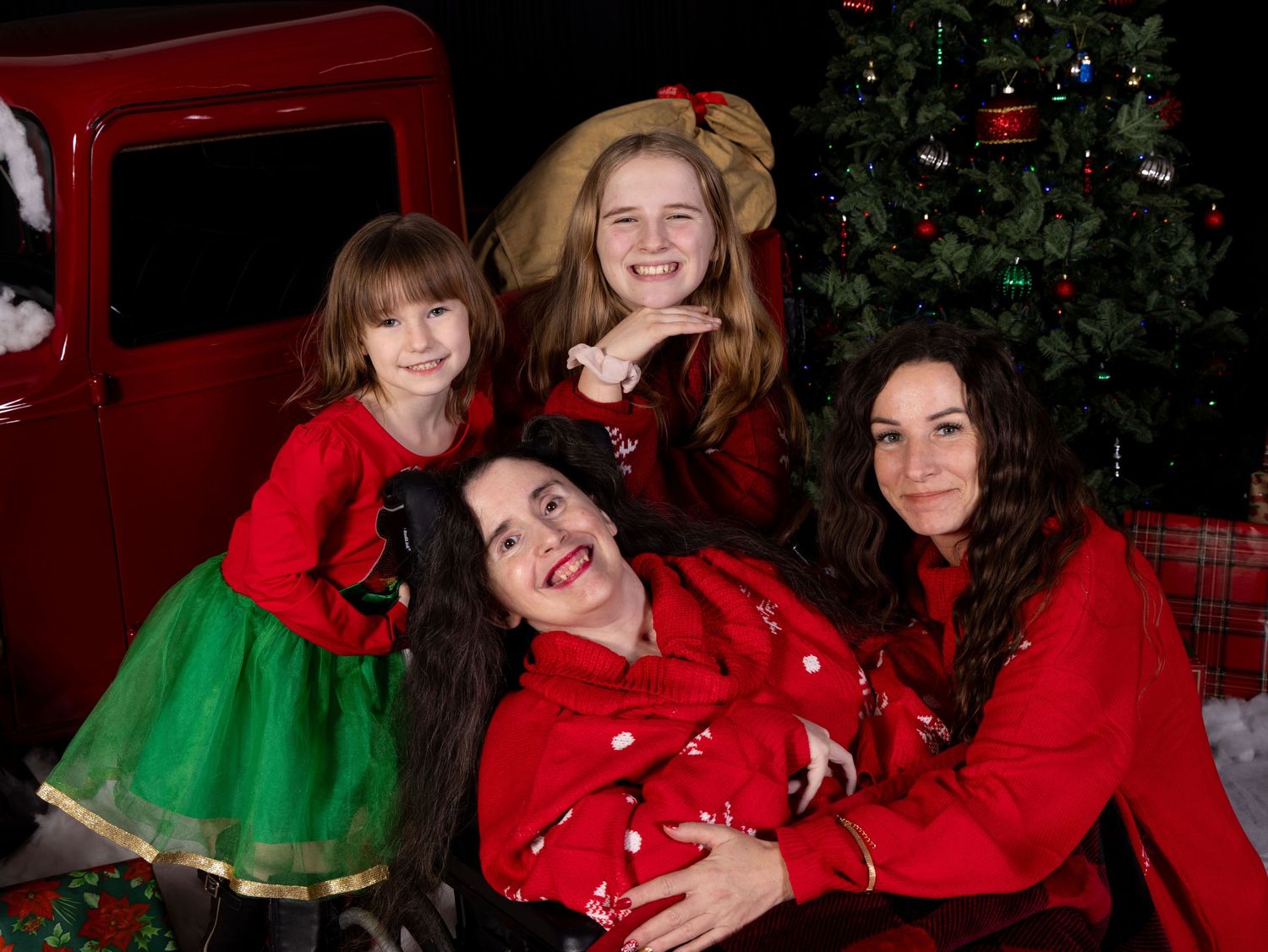 People wearing festive red and green outfits pose together in front of decorated Christmas trees.