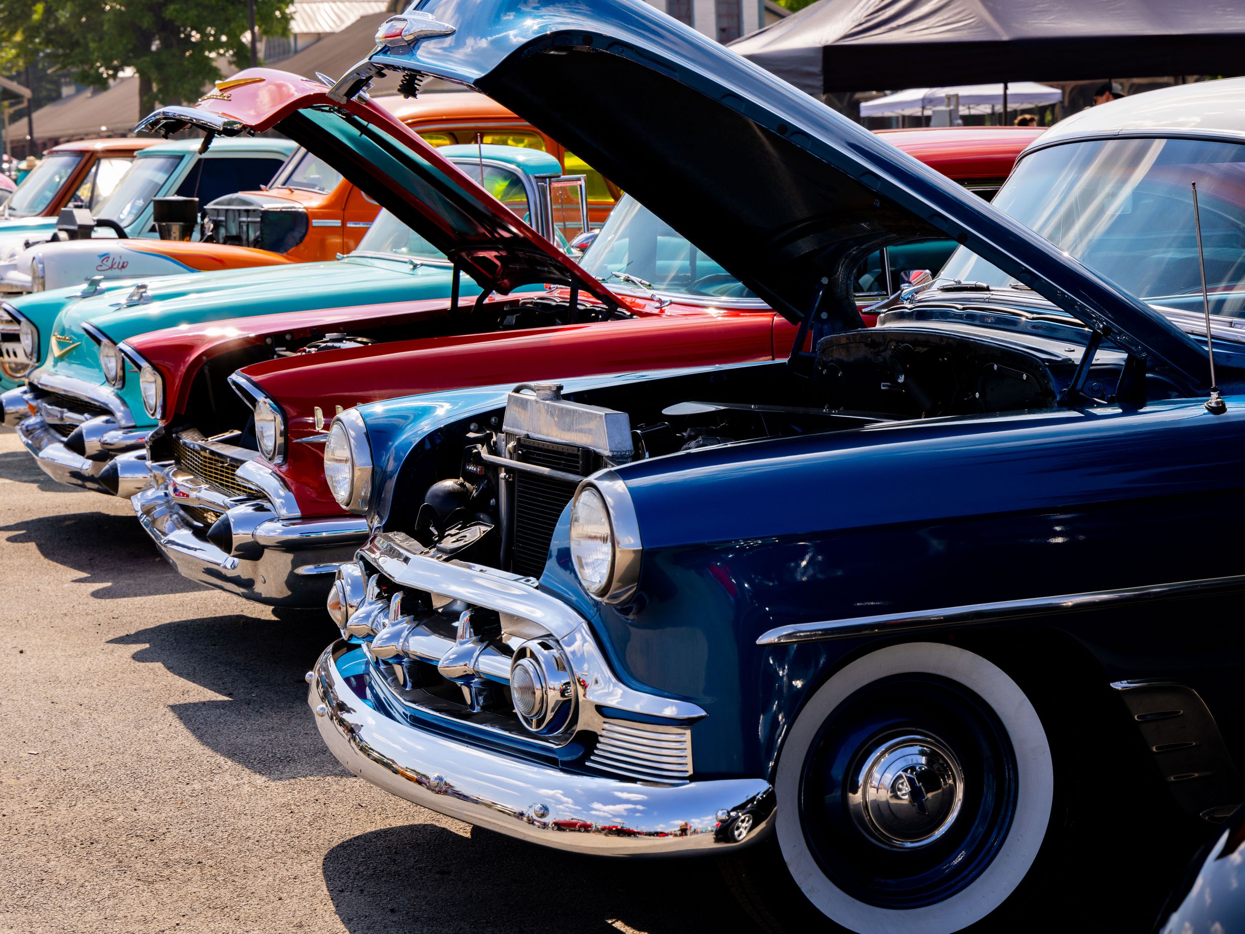 Row of vintage classic cars at an auto show with hoods open displaying engines.
