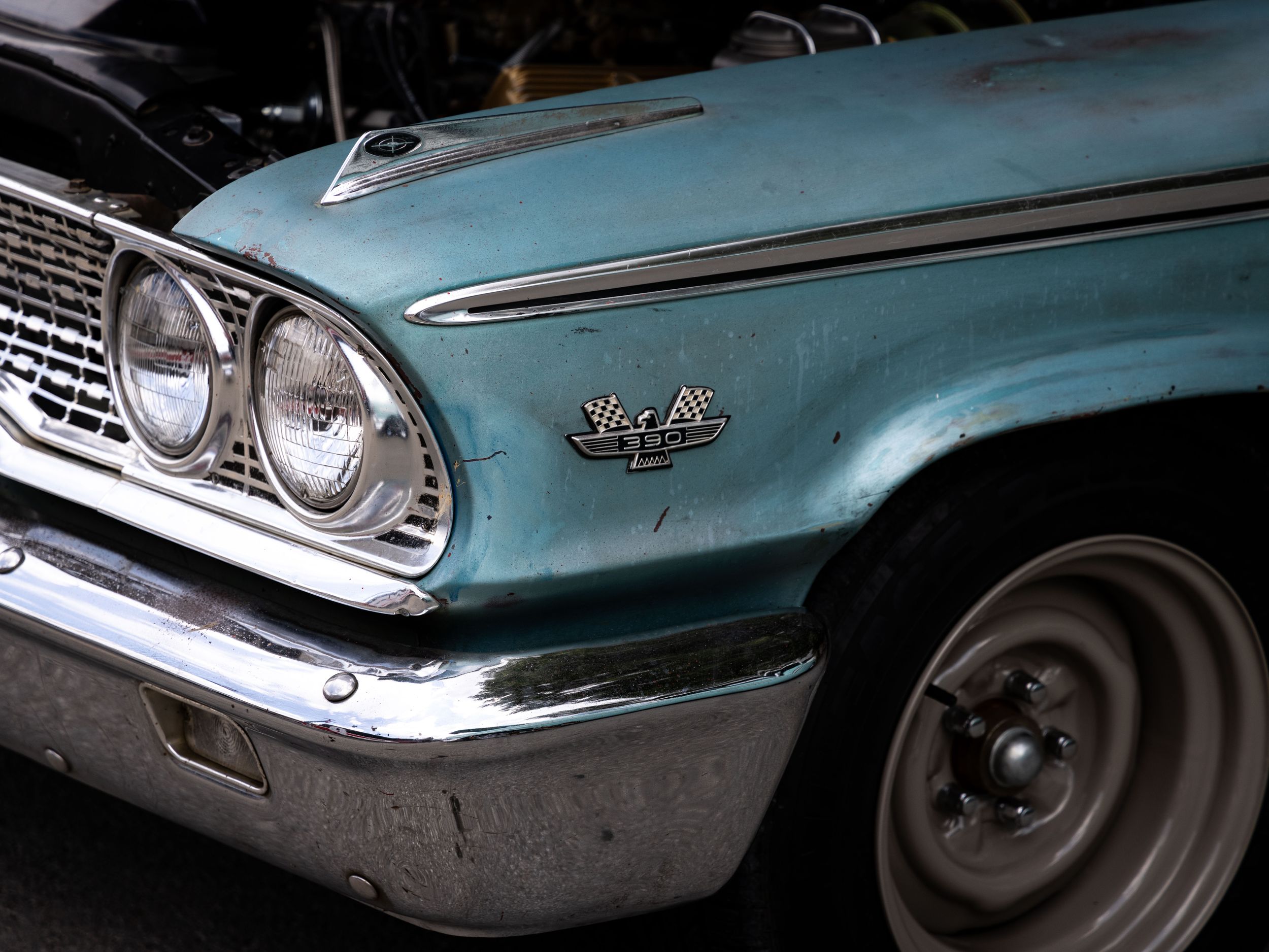 Close up of a turquoise vintage car front headlights and trim.