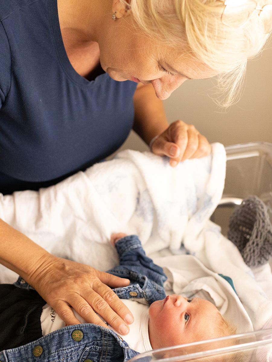 Grandmother lovingly gazes at newborn baby lying in hospital bassinet, tender family moment.