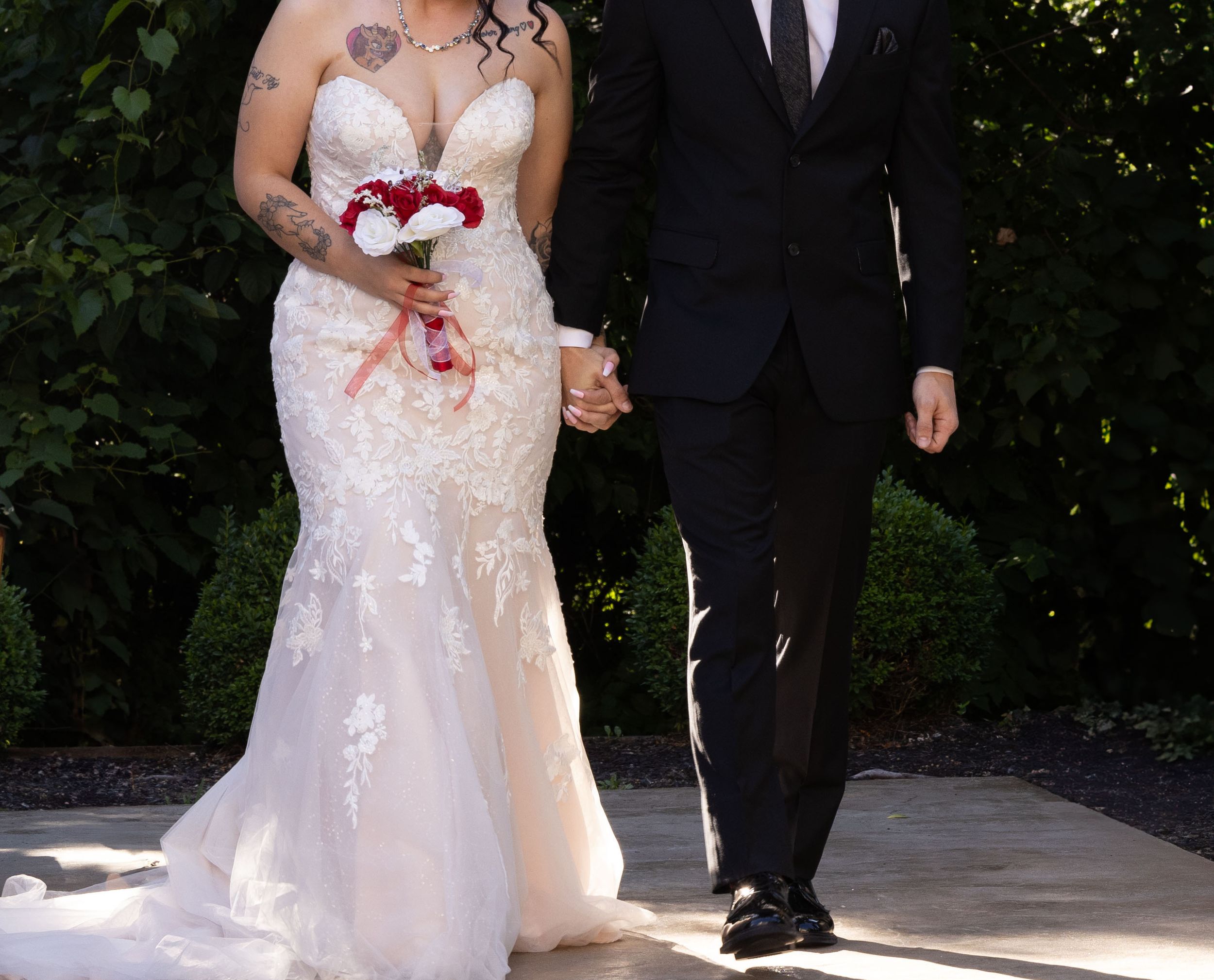A couple stands together during a wedding ceremony, with the bride wearing a fitted lace gown and holding a bouquet.