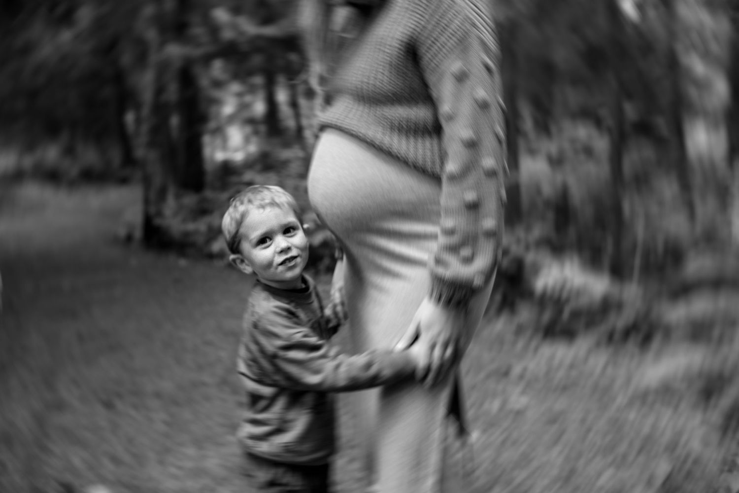 Black and white portrait of a small child embracing a parent in a forest setting.