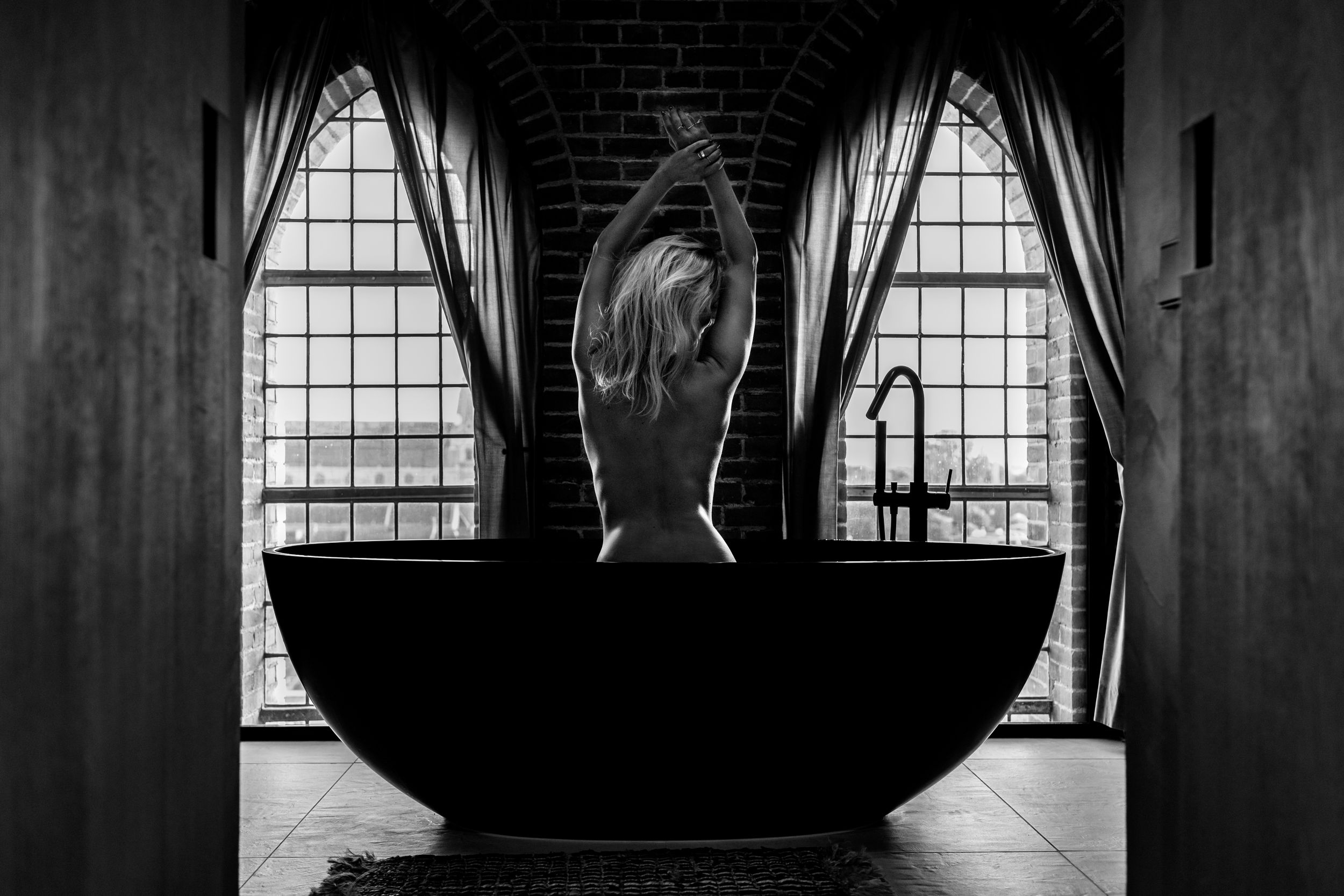 Moody architectural photo of a vintage bathroom with arched windows and freestanding tub.