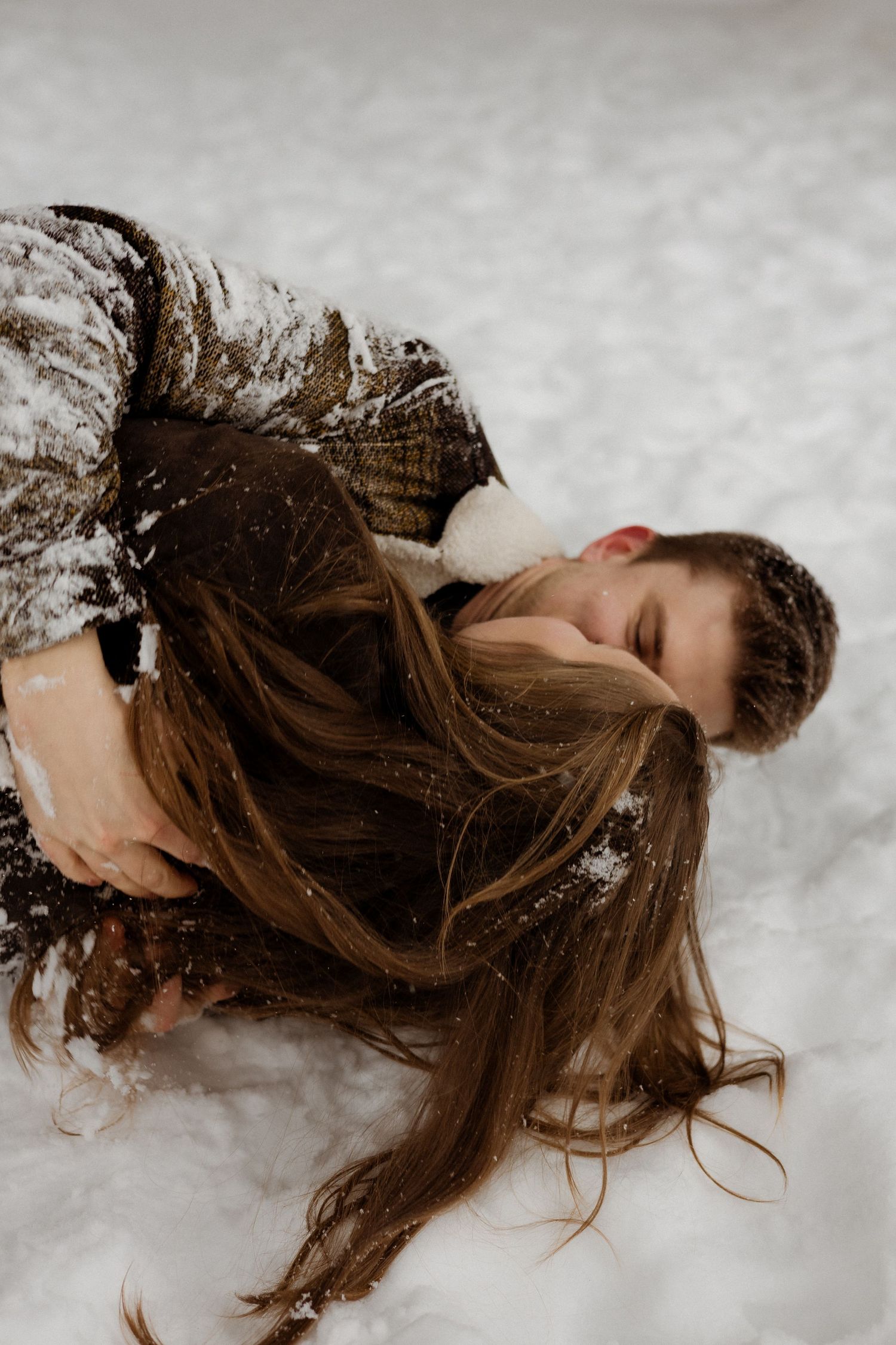 Long brown hair flows onto fresh white snow as someone lies back in winter weather wearing a knit sweater.