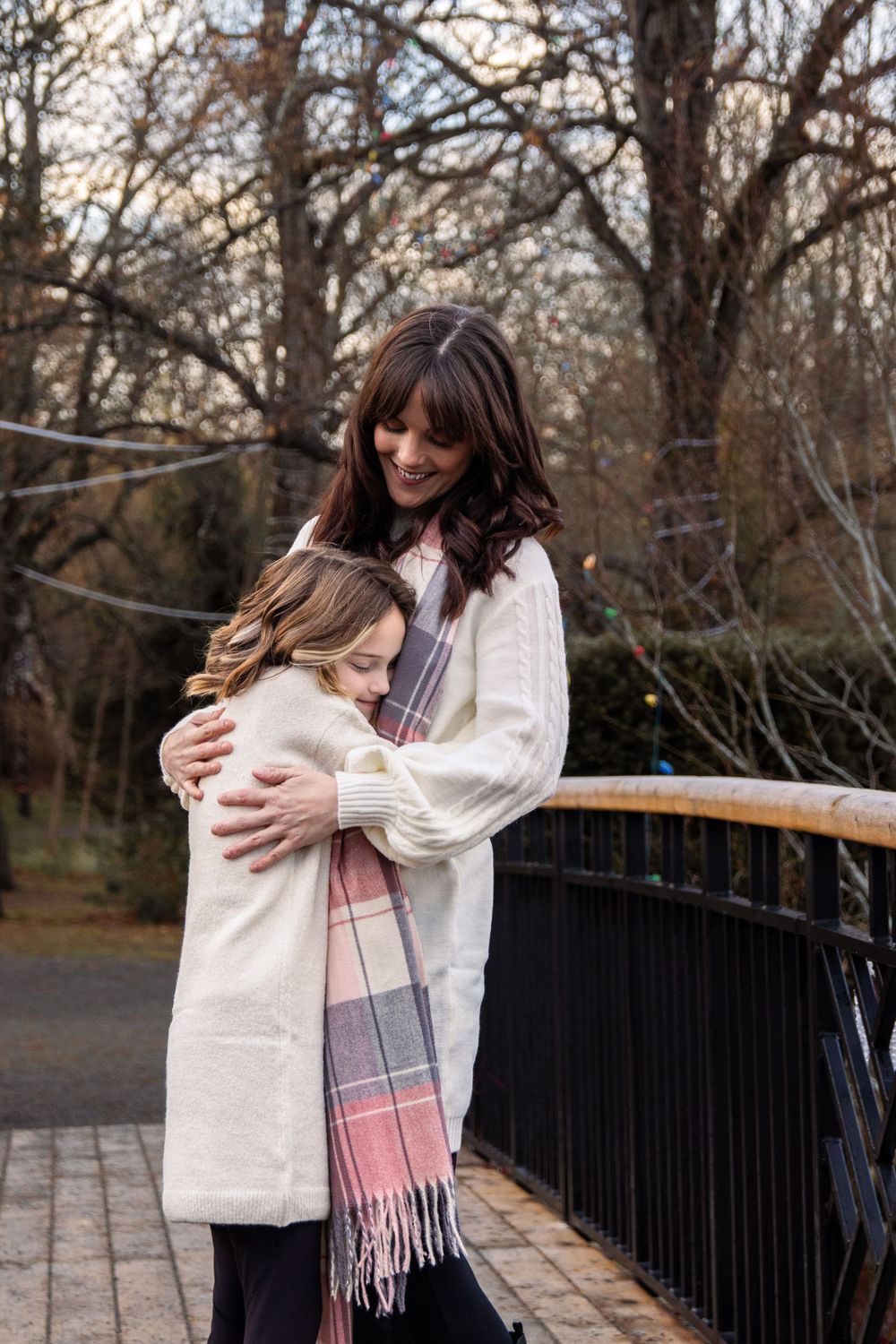 A tender embrace shared between parent and child on a bridge in a wooded autumn setting.