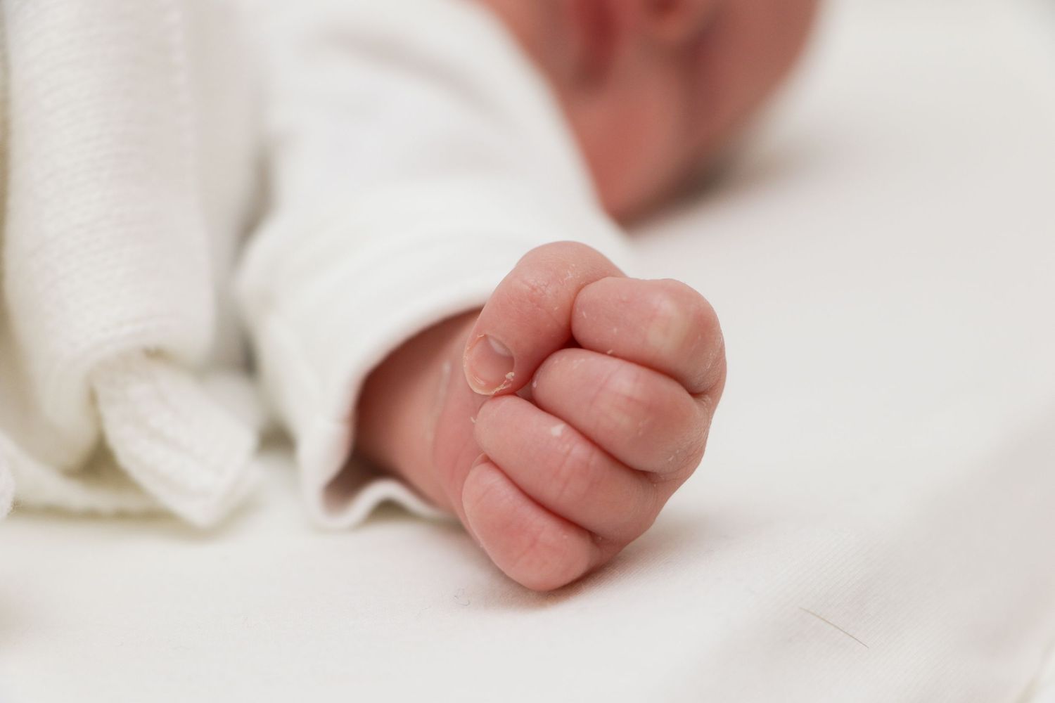 Close-up of tiny newborn baby's closed fist against white fabric.