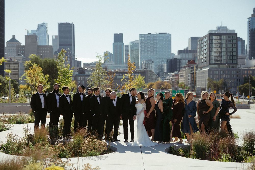 Group of business professionals standing in a line on a rooftop with city skyline and autumn foliage in background.
