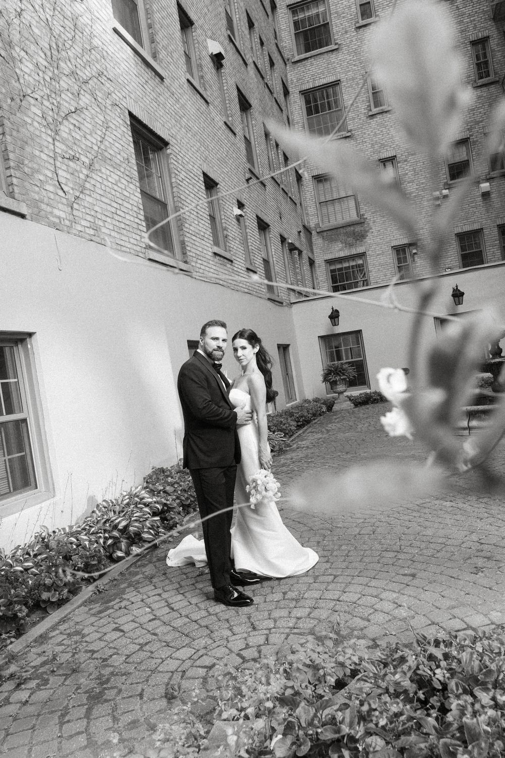 A series of black and white photos showing a couple walking along a cobblestone path between brick buildings.