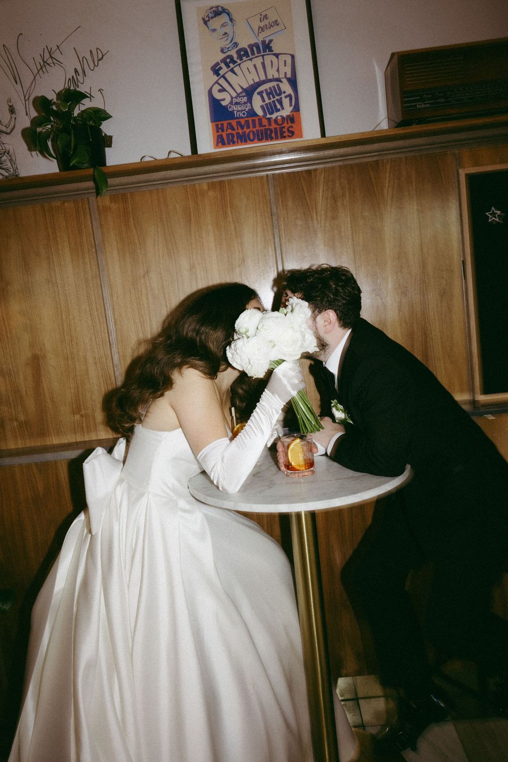 Four sequential photos show people in dark and light clothing leaning over a table in what appears to be a wood-paneled room.