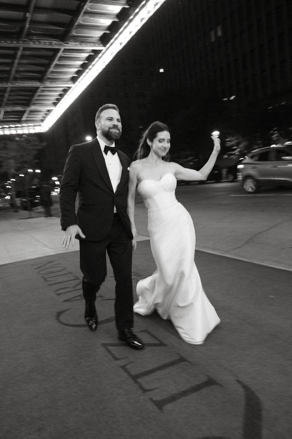 A black and white photo of a couple in formal wedding attire walking together outside at night.