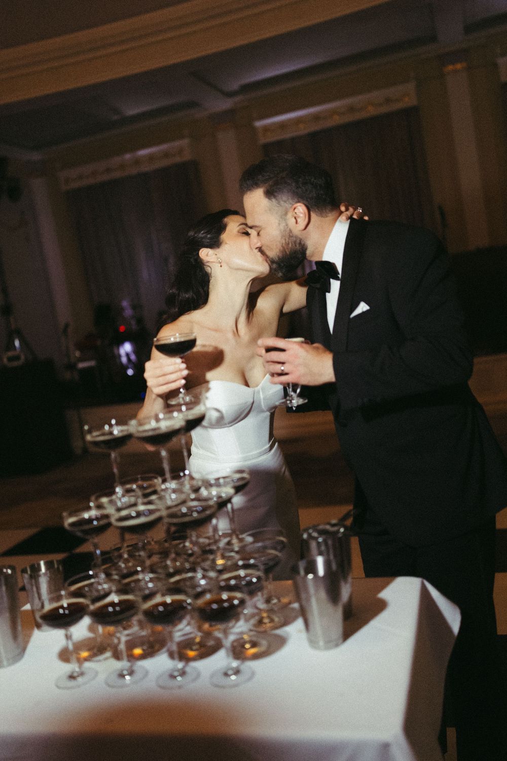 A couple shares a romantic kiss while performing a champagne tower pour at their wedding reception.