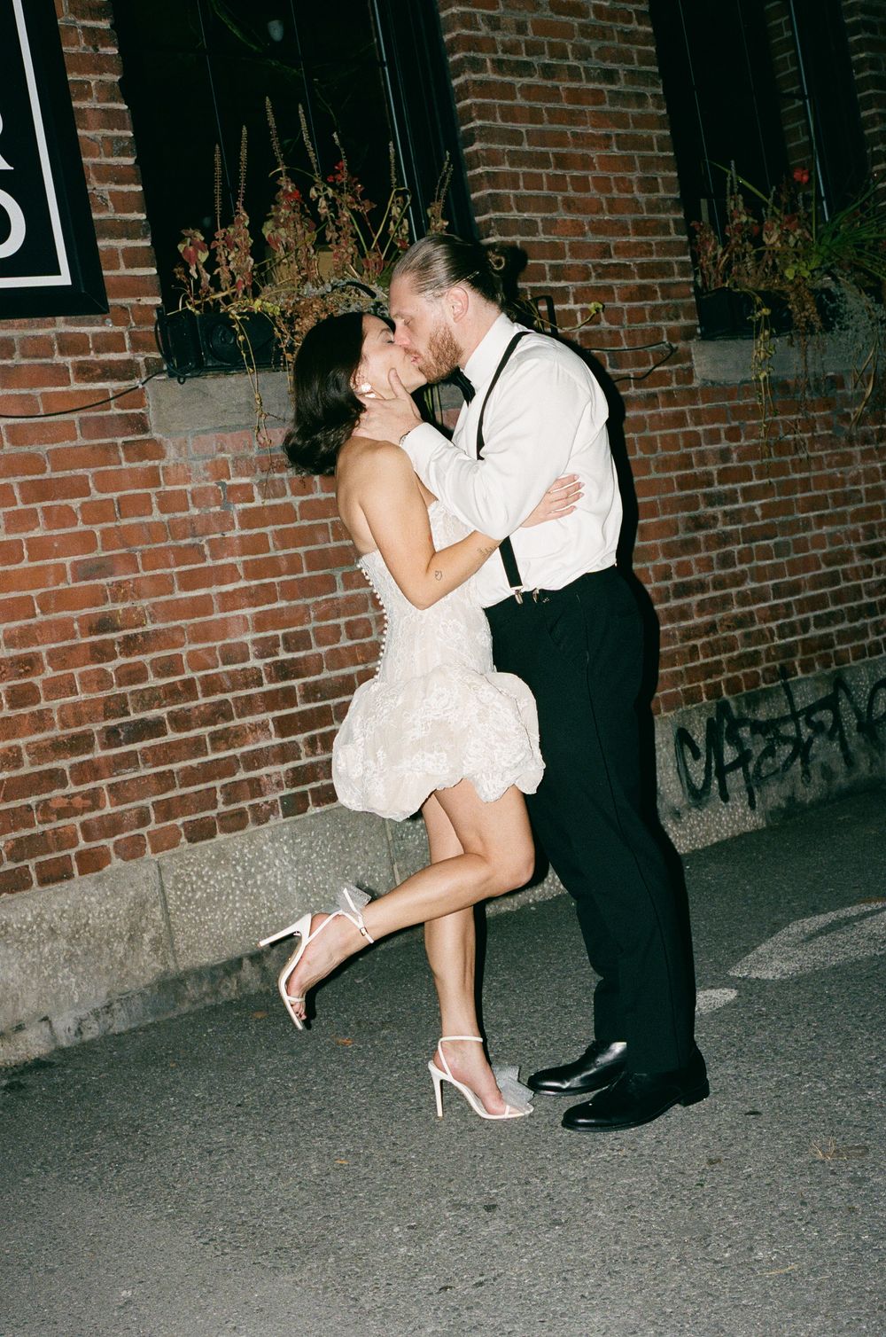 A romantic nighttime kiss against a brick wall background at a wedding celebration.