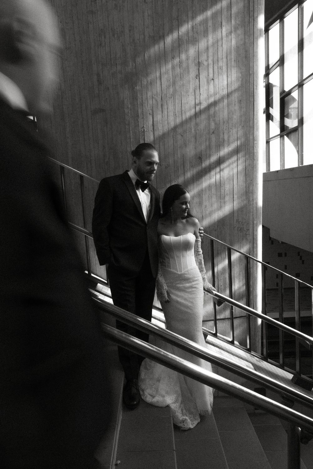 A couple descends a staircase in dramatic lighting during their wedding, creating a cinematic black and white moment.