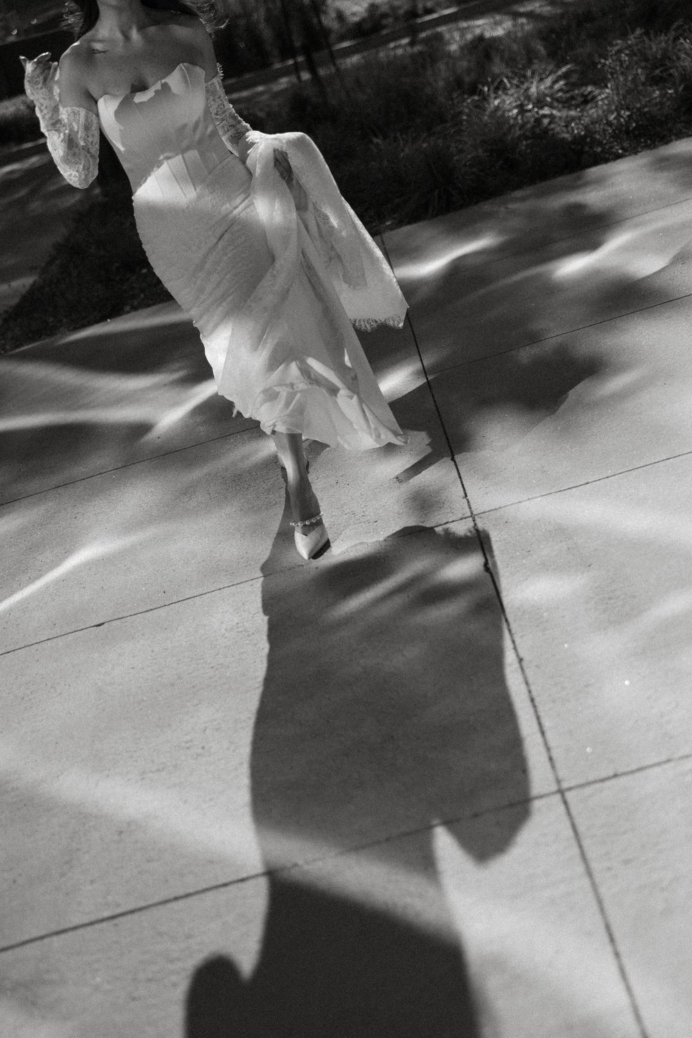 Black and white photo of a bride in a flowing dress casting dramatic shadows on a tiled floor.