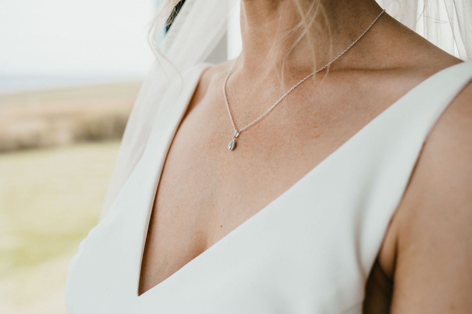 Close up detail of delicate silver necklace on bride wearing white v-neck wedding dress.