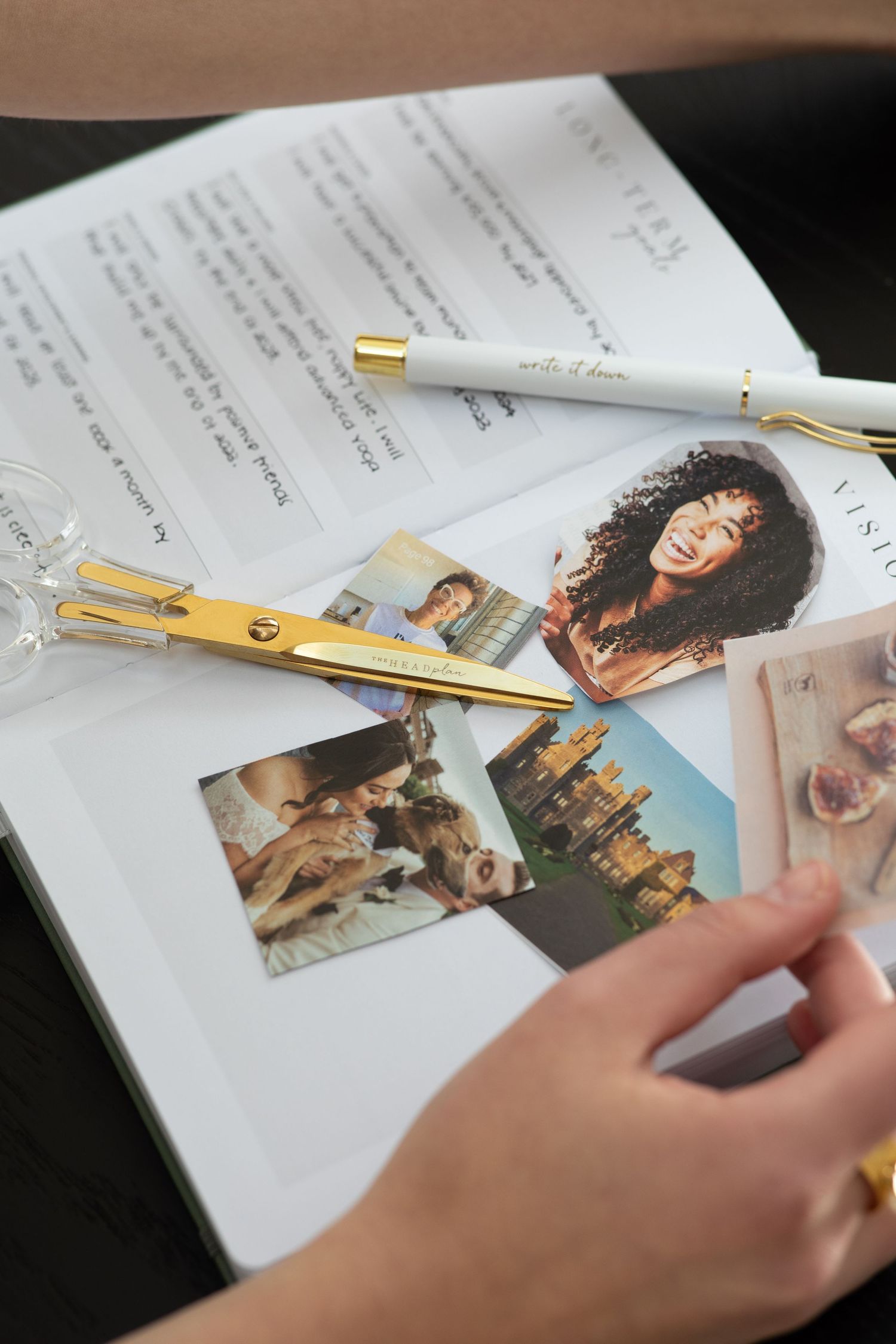 An open planner with photographs and a white pen arranged on a dark surface.