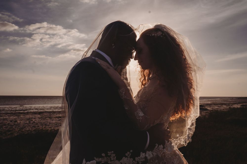 Silhouetted couple embracing at sunset on a beach with sunlight glowing through their hair.