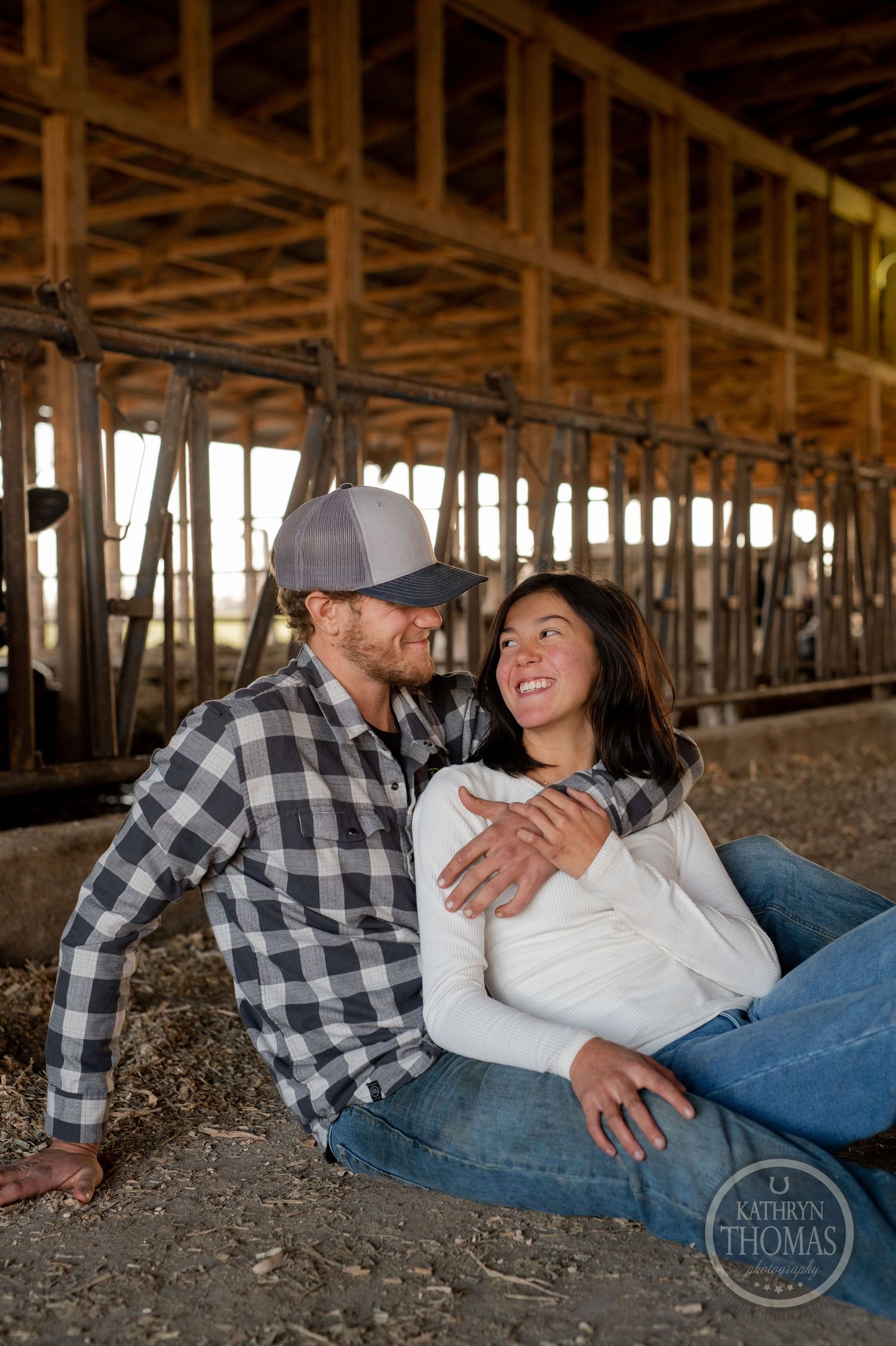 A romantic moment captured between a couple sitting beneath wooden barn rafters.
