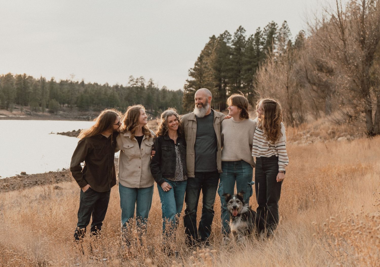 Group walking along autumn path near lake shore in casual fall attire during golden hour sunset.