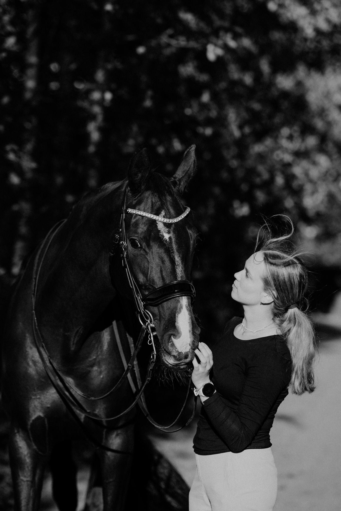 A heartwarming black and white photo of a rider in a black sweater sharing a tender moment with their dark horse.