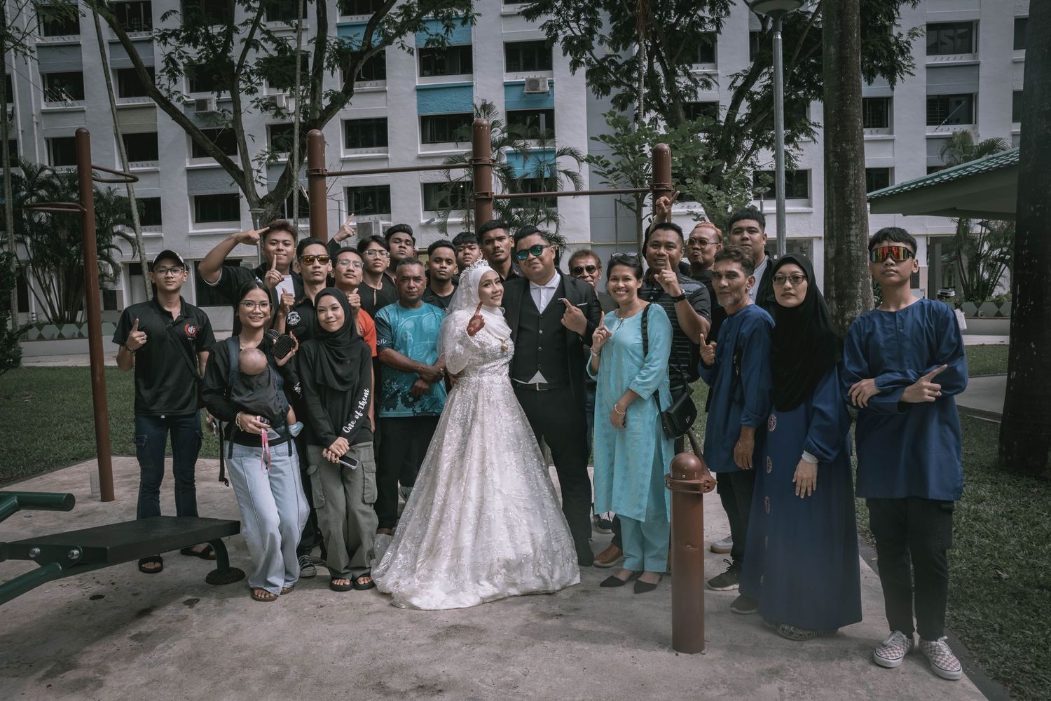 Large group wedding photo with guests outdoors in casual and formal attire.