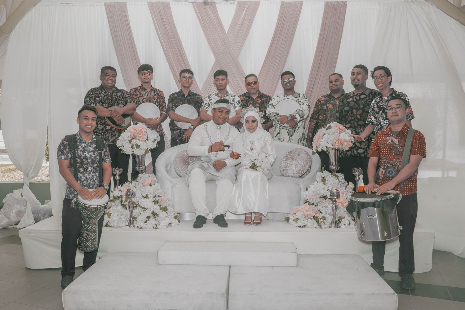 Group photo of wedding party members standing together in decorated white tent venue.