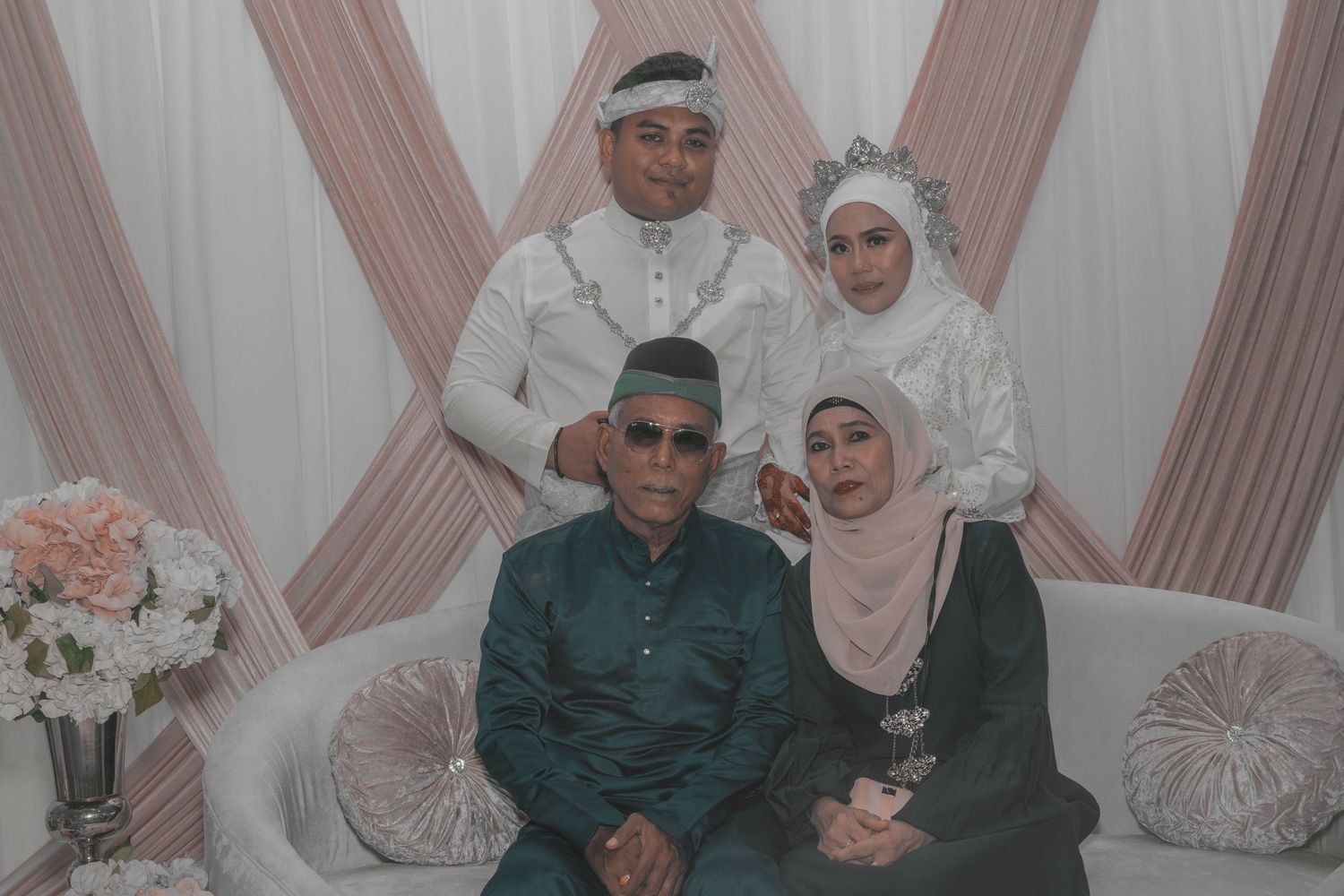 Family portrait with two couples in traditional formal attire against draped backdrop.