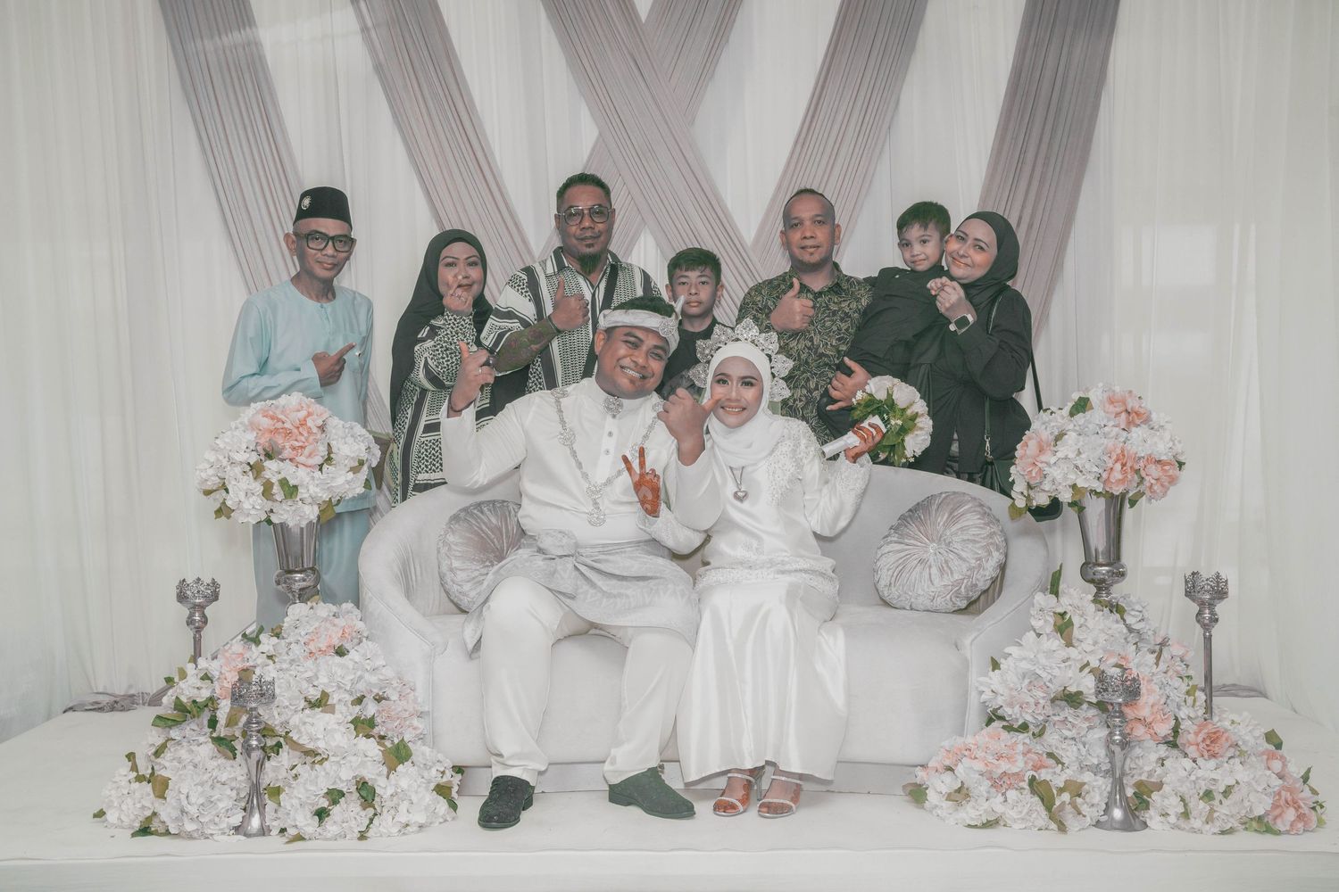 Wedding party group photo with bride and groom seated center surrounded by family in formal attire.