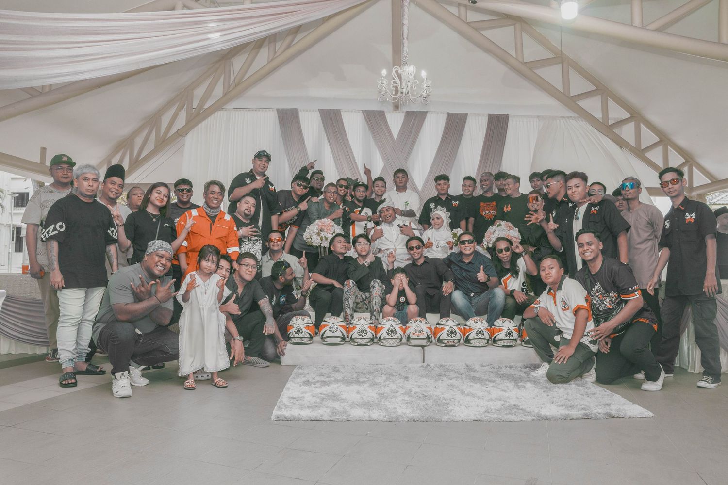 Large group photo of wedding guests and family members gathered in decorated reception venue.